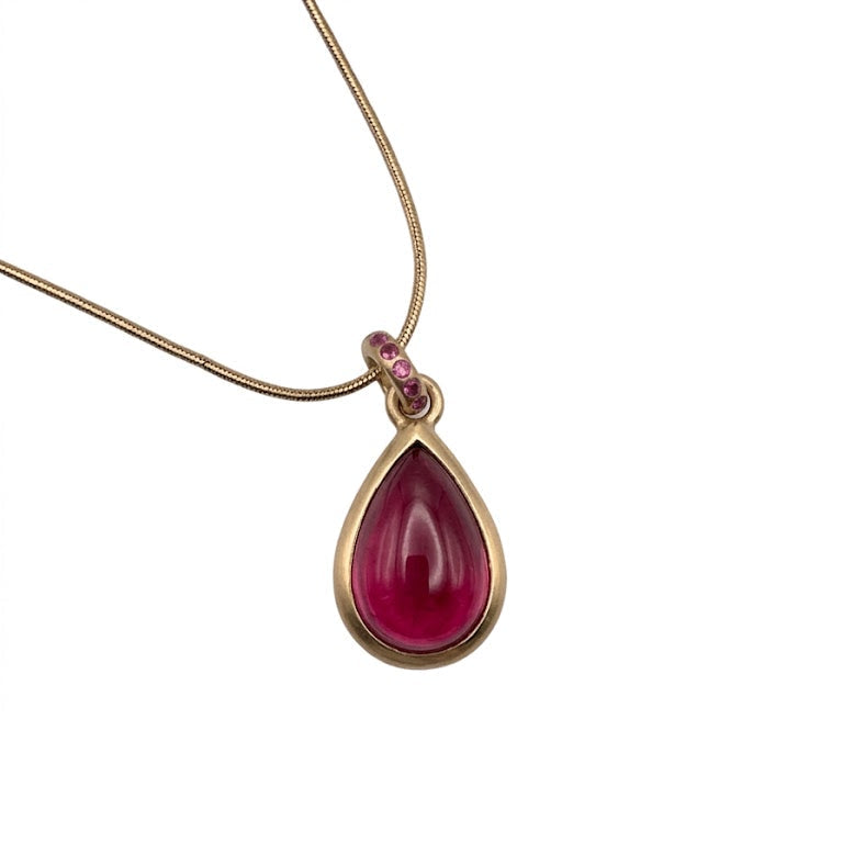 Teardrop Raspberry Tourmaline Pendant in Gold — A luscious deep raspberry teardrop Tourmaline cabochon is set in a solid 14K, with accent round bail covered with pink sapphires